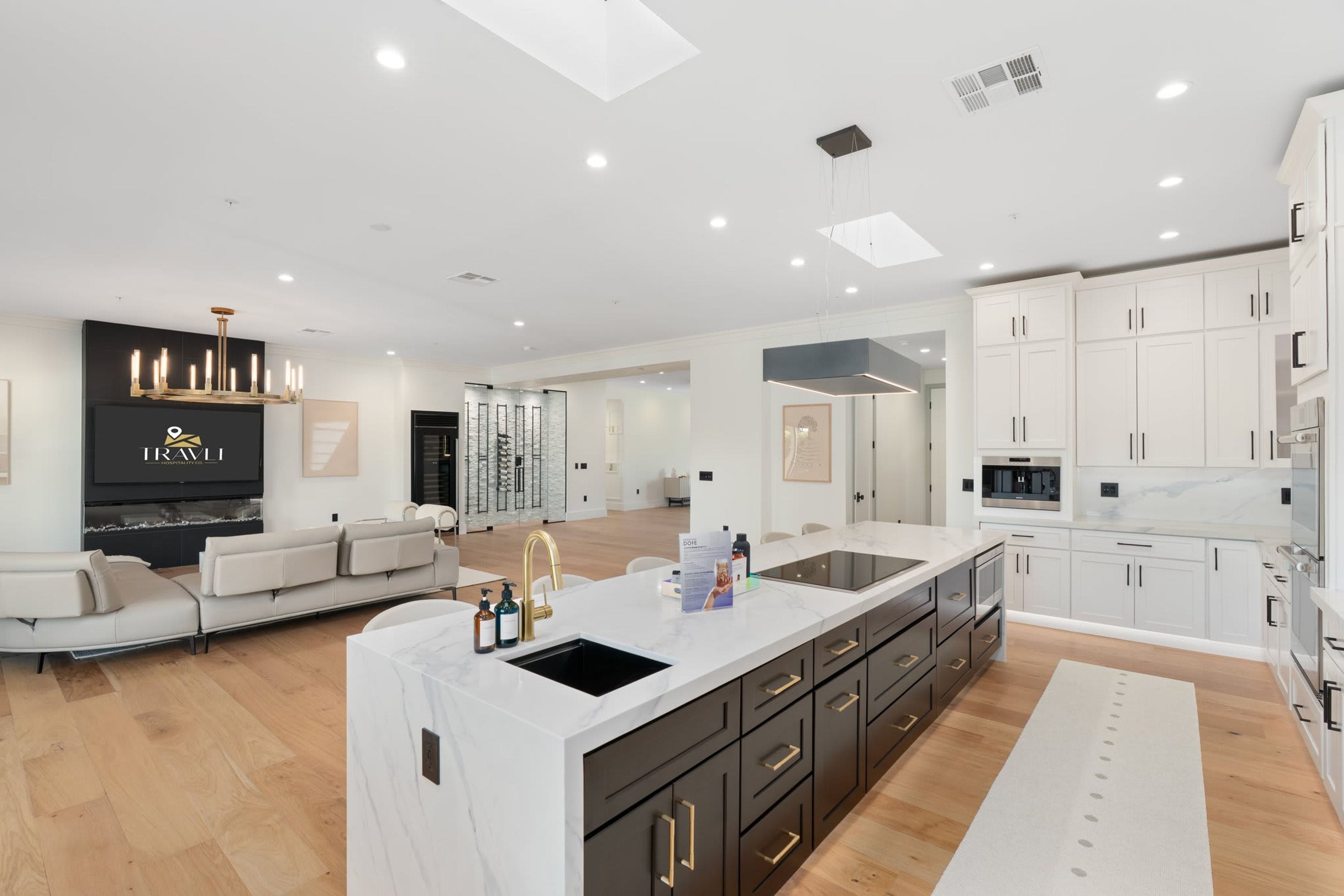 A modern kitchen with a large island, white cabinetry, and a built-in oven.