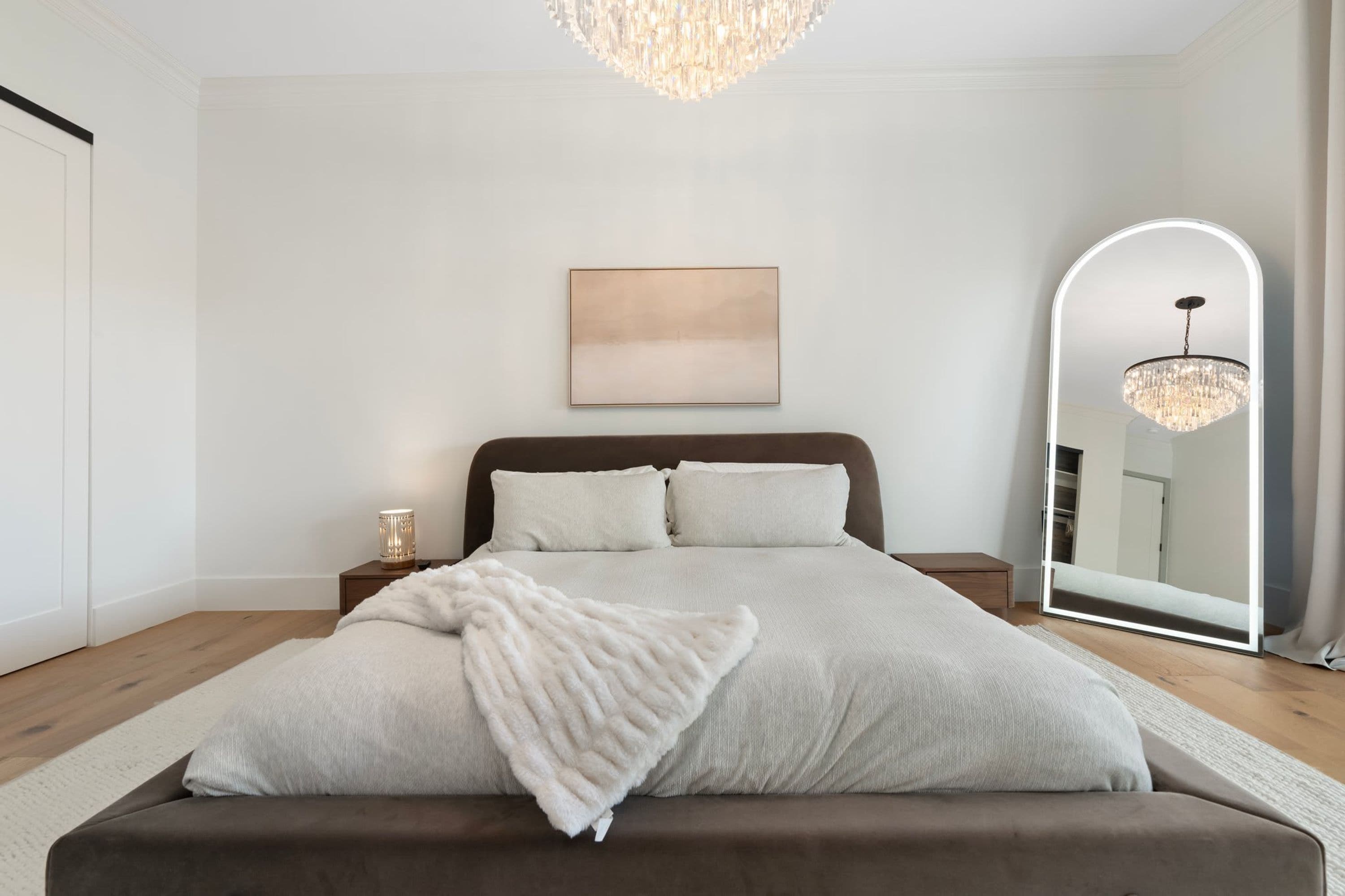 A bedroom with a large bed, a bedside table, a mirror, and a chandelier.