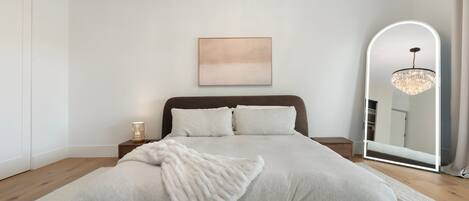 A bedroom with a large bed, a bedside table, a mirror, and a chandelier.