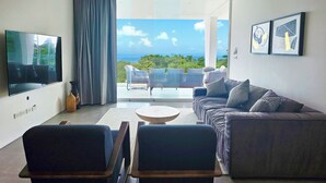A modern living room with a flat-screen TV, a ceiling fan, a sofa, two armchairs, and a coffee table.
