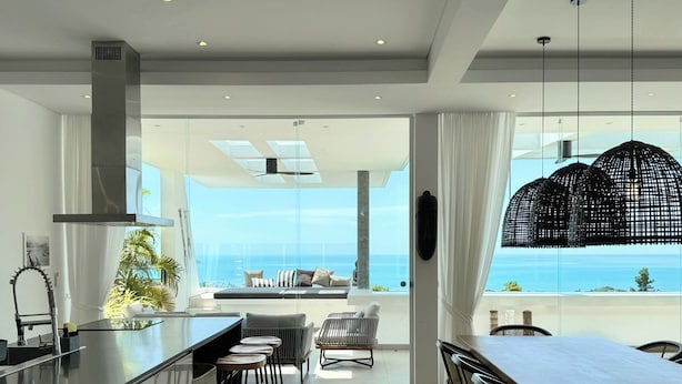 A modern kitchen with a large island, bar stools, and a dining area with a view of the ocean.