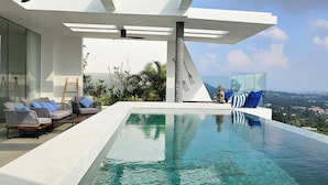 A modern infinity pool with a Buddha statue, outdoor seating, and a clear view of the city skyline.