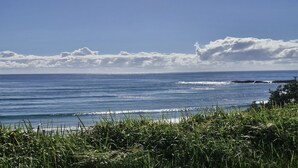 Paisagem costeira com vista para o oceano, ondas e um primeiro plano gramado.