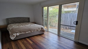 A bedroom with a bed, a sliding glass door, and a wooden floor.