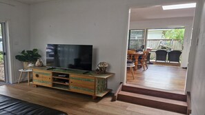 Un soggiorno con televisione, un mobile porta TV in legno e una scala che conduce a una zona esterna con tavolo e sedie.
