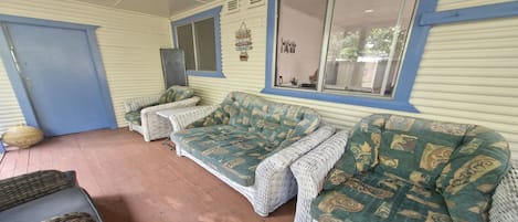 A covered outdoor seating area with wicker furniture and a blue door.