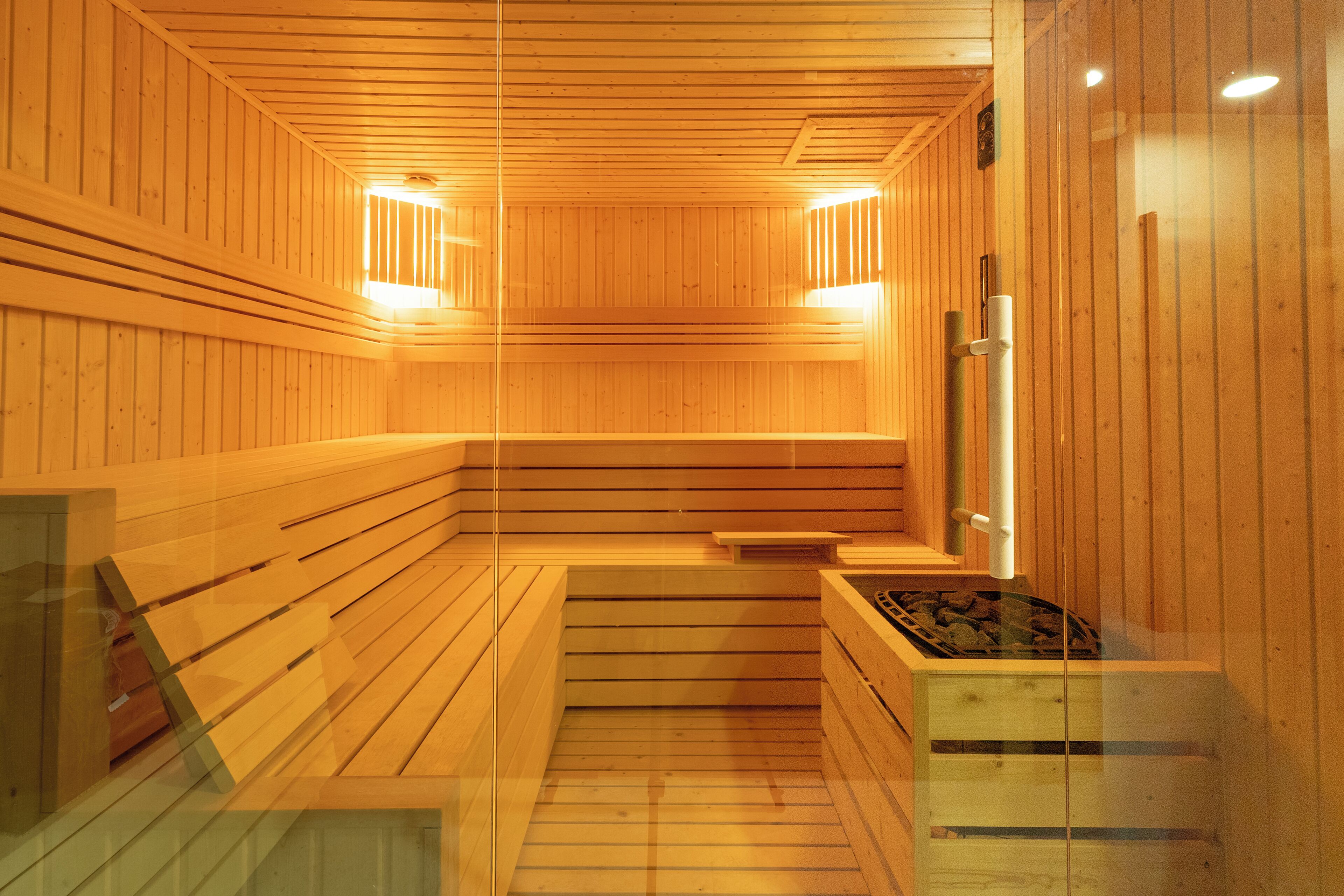 Un sauna aux murs et aux bancs en bois, avec un banc au centre et une petite table équipée d’un radiateur.