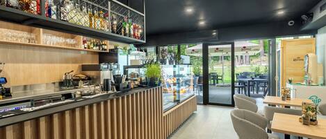 Un área de bar moderna con mostrador de madera, estantes llenos de botellas y una vitrina de cristal.