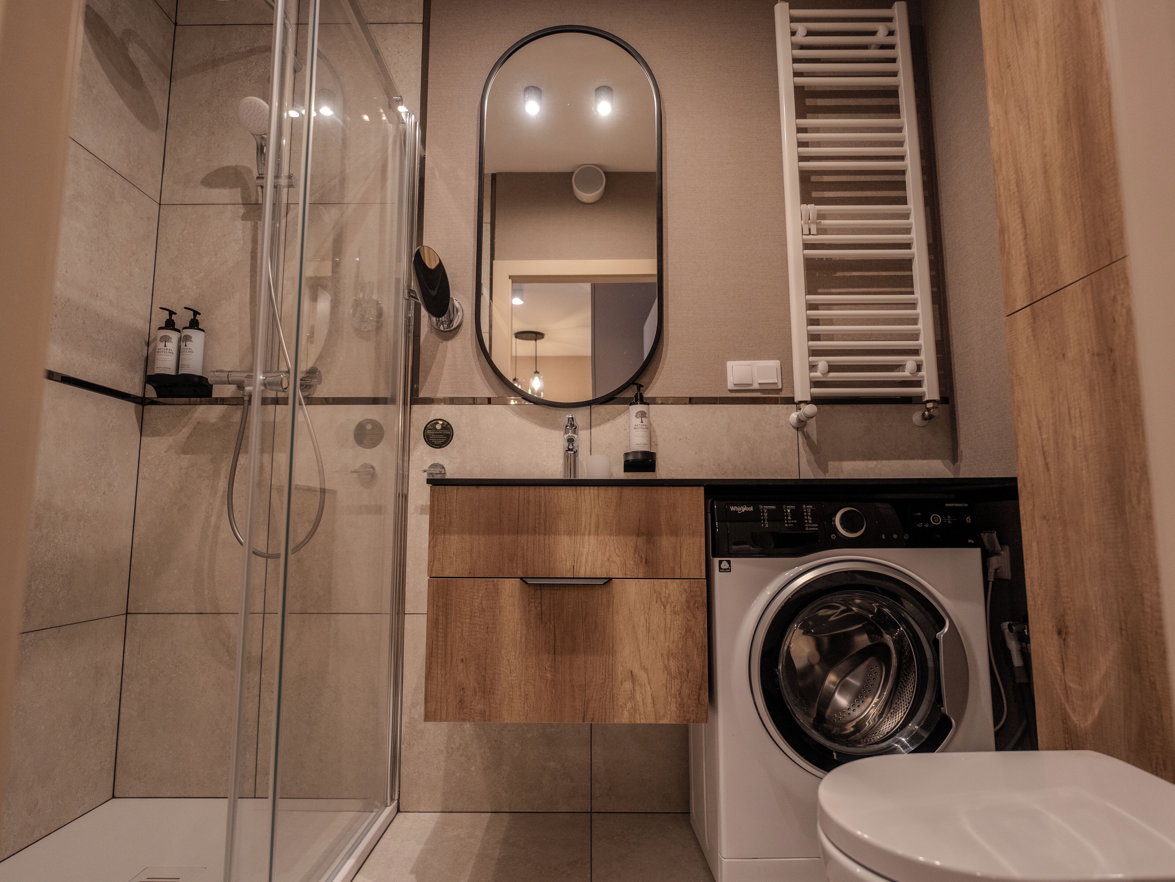 A modern bathroom with a glass shower enclosure, a built-in washing machine, and a toilet.