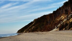Uma praia com um morro arborizado e uma escadaria subindo.
