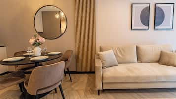 Un salon moderne avec un canapé beige, une table de salle à manger ronde entourée de chaises, un grand miroir et deux œuvres d’art encadrées accrochées au mur.