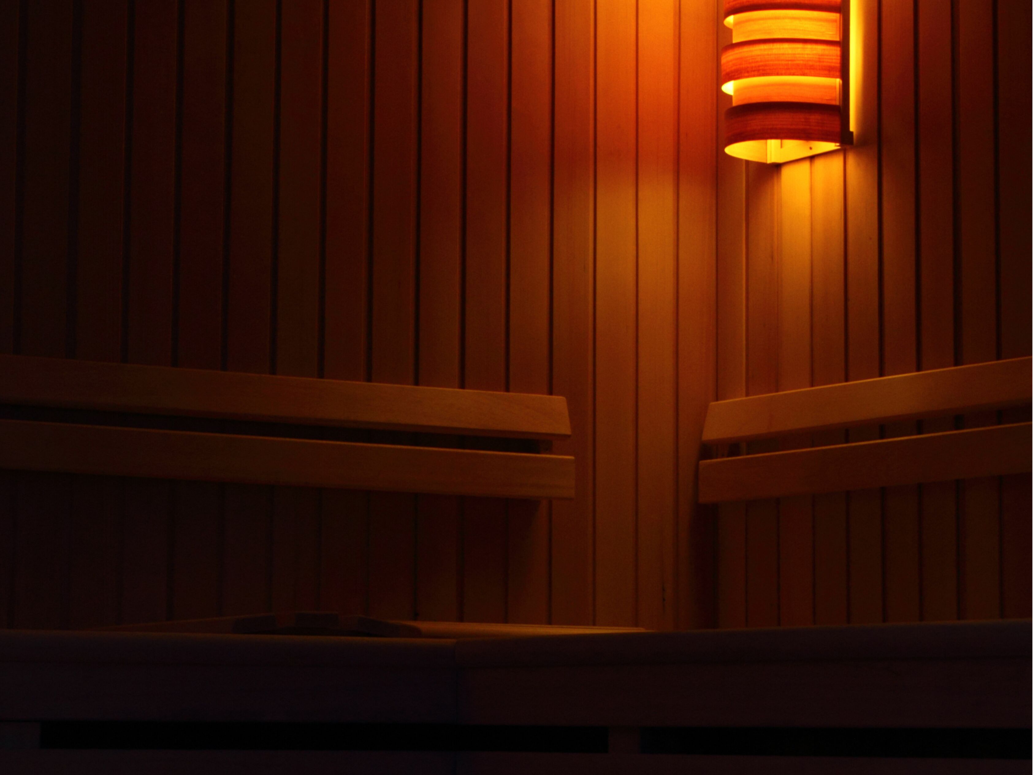 A wooden bench with a backrest and armrests, positioned against a wall with vertical wooden slats.