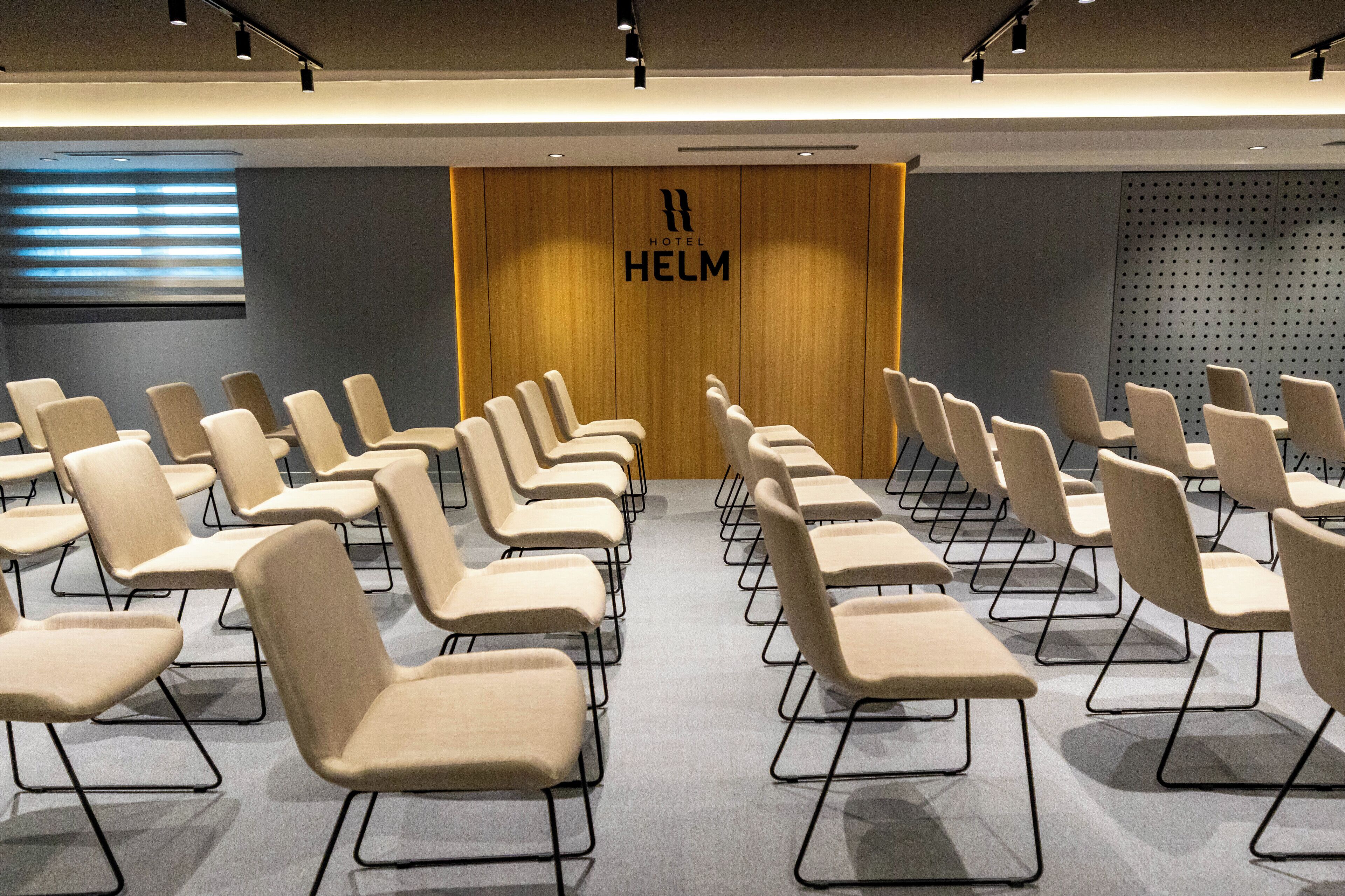 Un salón de conferencias de hotel con hileras de sillas color beige y una pared de madera con el nombre del hotel.