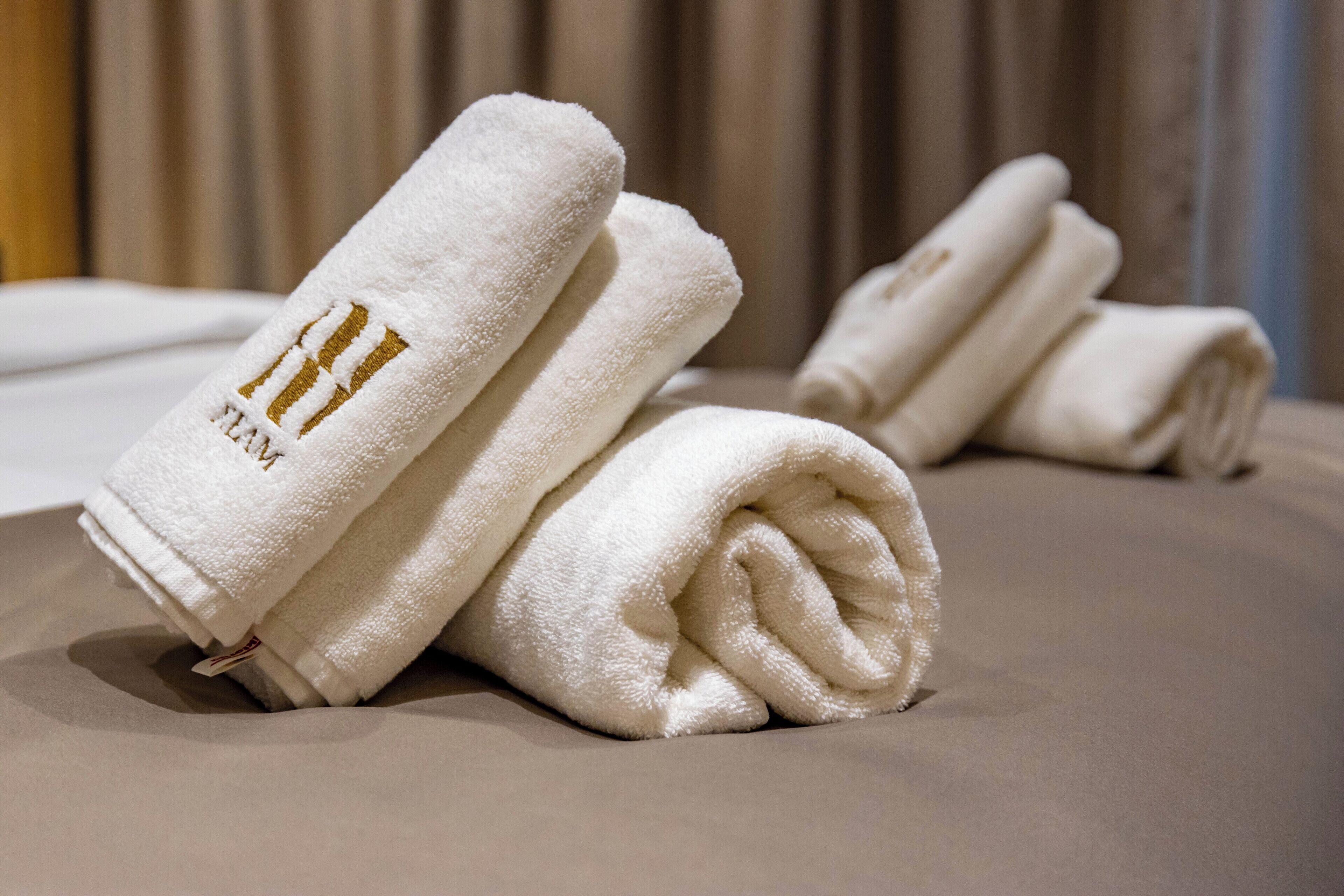 Des serviettes blanches, soigneusement pliées, ornées d’un écusson doré, sont posées sur le lit.