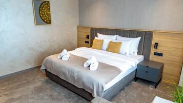 A modern hotel room with a large bed, a nightstand, a small table with a plant, and a wall art piece.