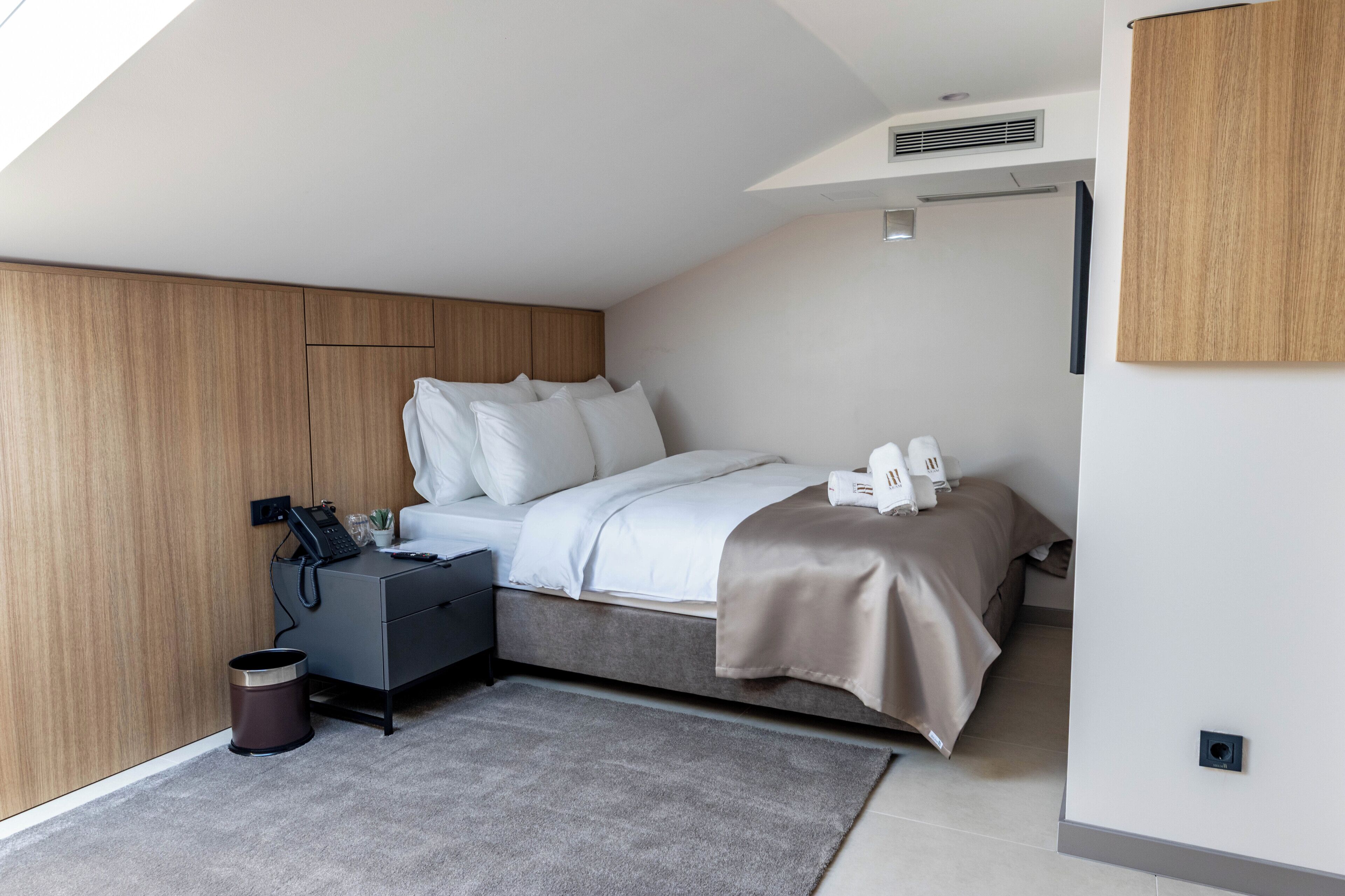 A modern bedroom with a bed, bedside table, and a small trash bin.