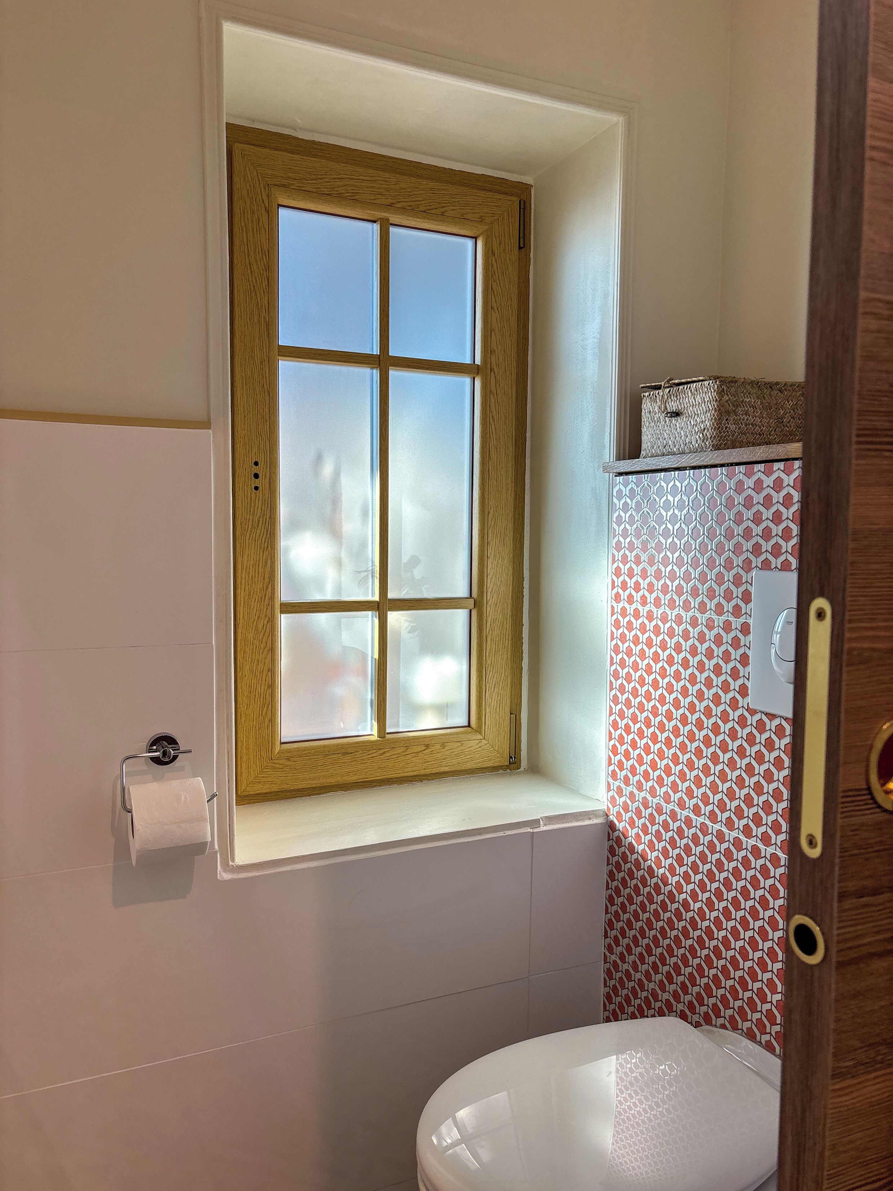 Une salle de bain avec une fenêtre, des toilettes et des carreaux décorés.