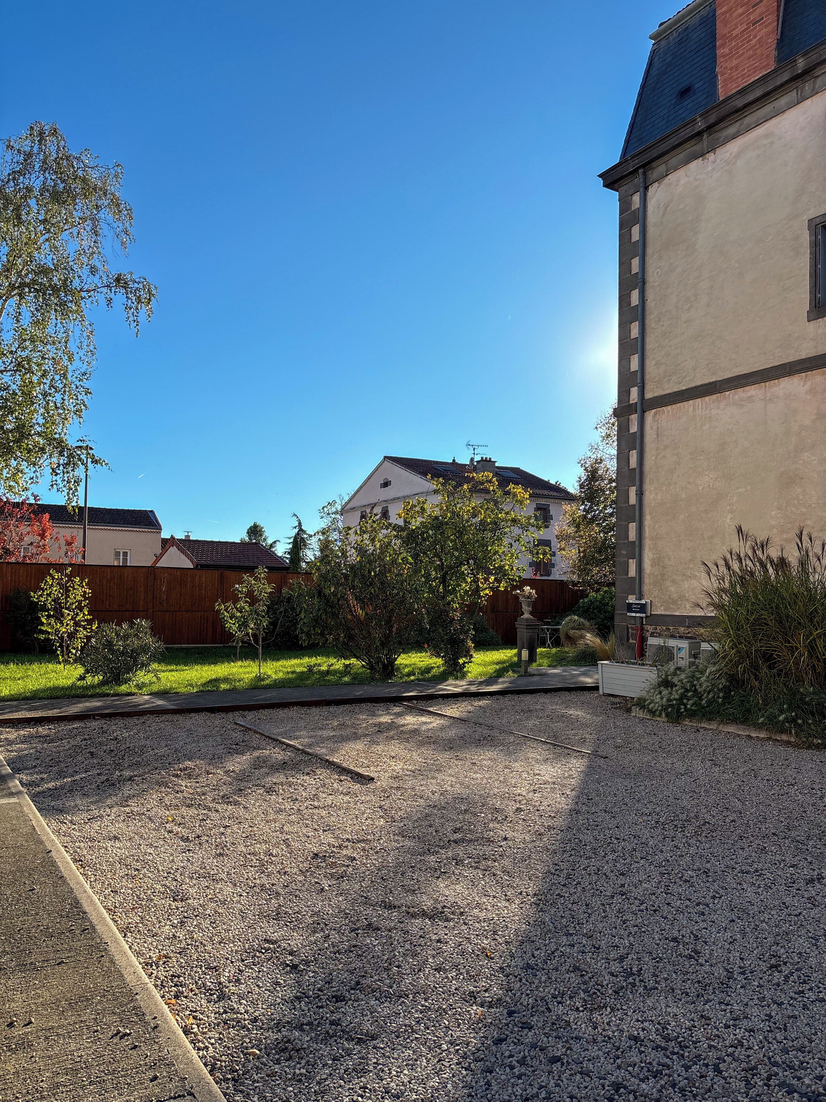 A residential area with a gravel driveway, a wooden fence, and a building with a tiled roof.