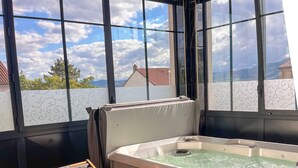 Een hottub met uitzicht op de lucht en gebouwen, houten lounge fauteuils en een betegelde vloer.
