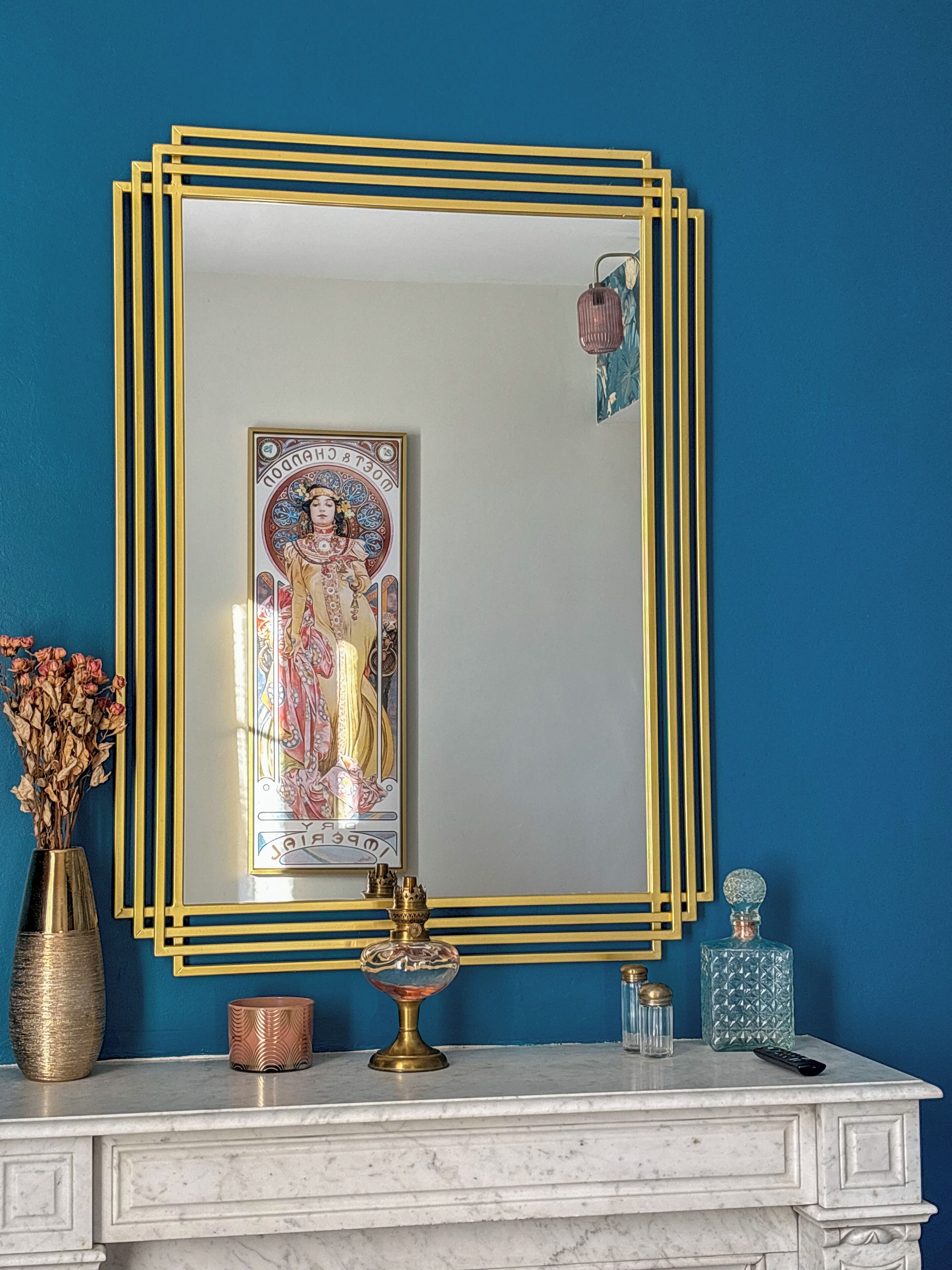 Un bagno con una parete blu, un lavabo in marmo bianco, uno specchio con cornice dorata e oggetti decorativi tra cui fiori secchi e un vaso.