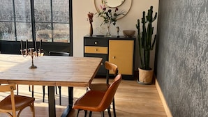 Een eethoek met een houten tafel en stoelen, een zwart en gouden kast, een groot raam en een cactus.