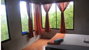 Ein Zimmer mit einem Bett, einem Vorhangfenster und Blick auf Grünfläche.