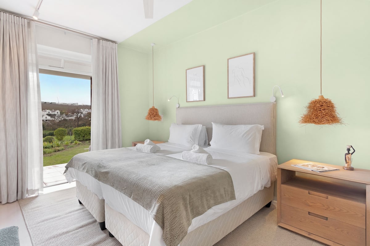A bedroom with a large bed, a nightstand, a window with curtains, and two framed pictures on the wall.