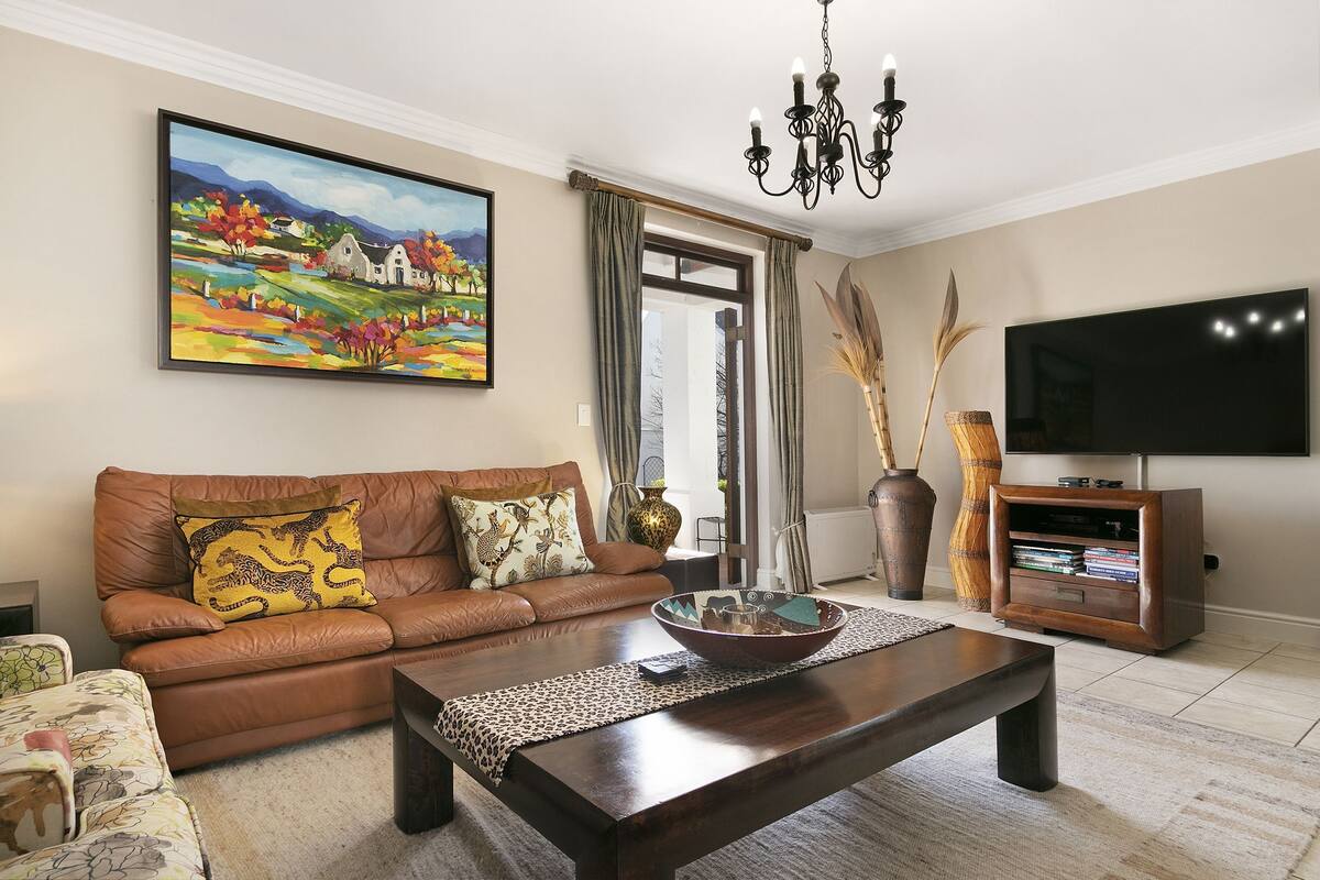 A living room with a brown leather sofa, a wooden coffee table, a flat-screen TV, and a painting on the wall.