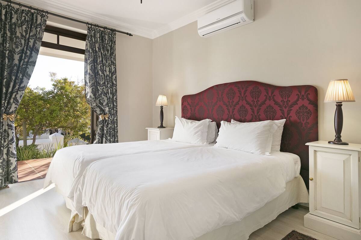 A large bed with white linens, a red headboard, and two bedside lamps.