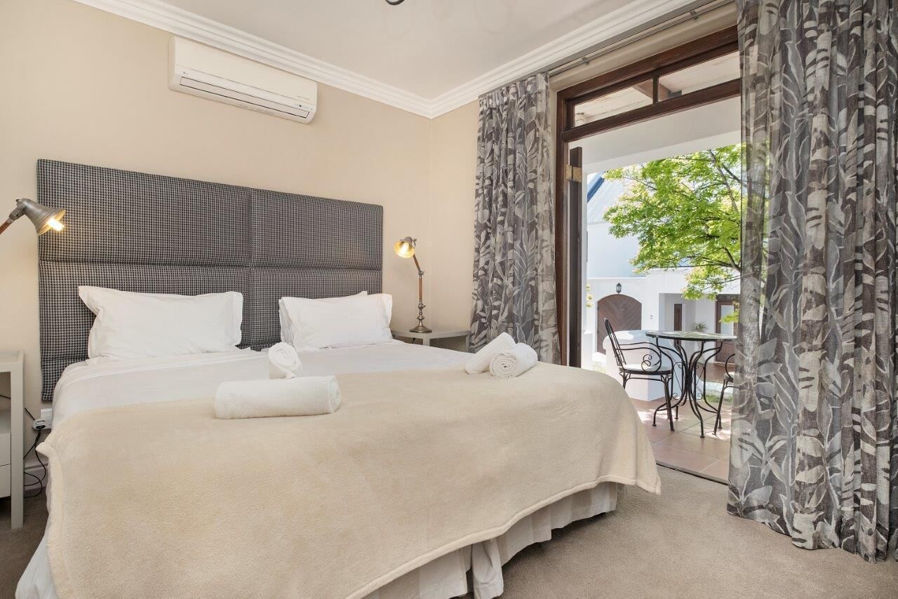 A hotel room with a large bed, a headboard, a bedside table, a lamp, and a view of the outside.
