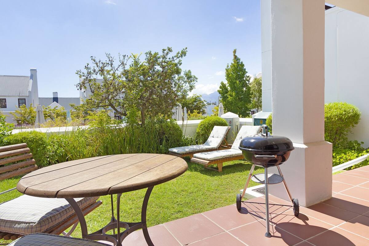 A patio with a table, two lounge chairs, and a barbecue grill.