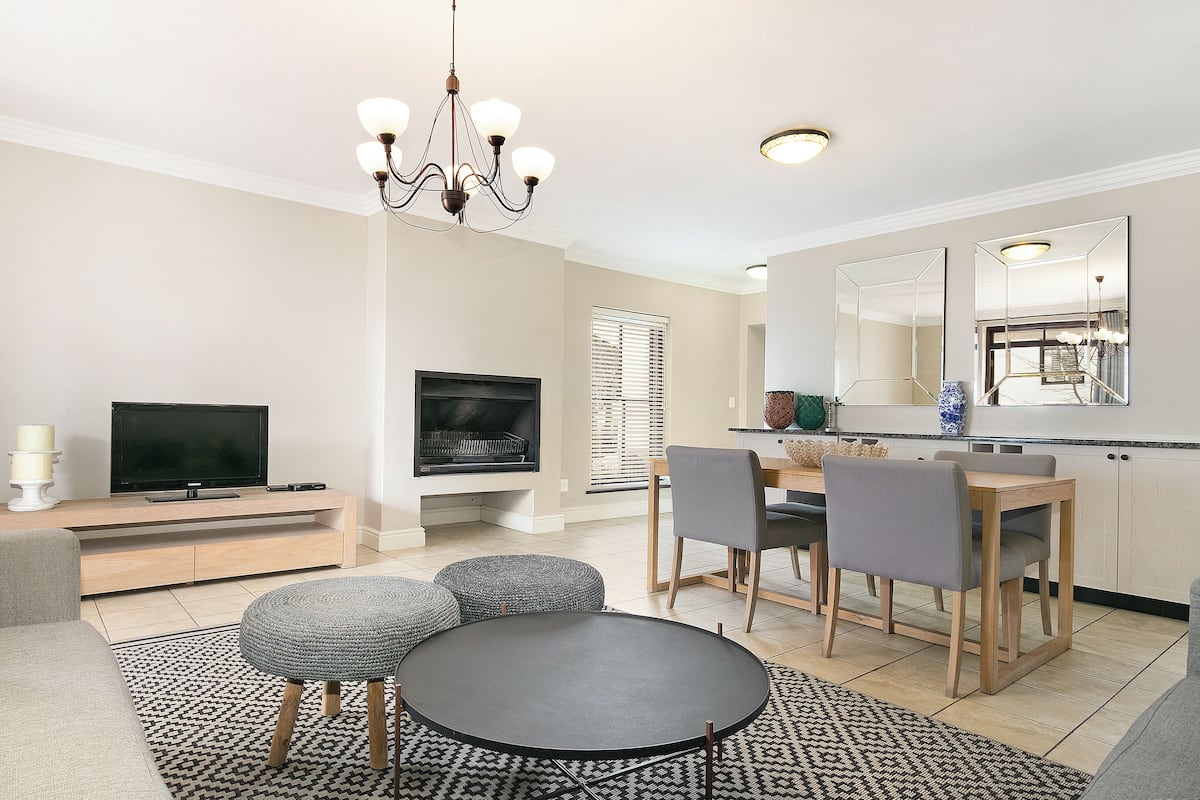 A modern living room with a TV, sofa, ottomans, and a dining area with chairs and a table.