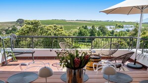 Eine Terrasse mit Blick auf Weinberge, Gartenmöbel und einem Metallgeländer.