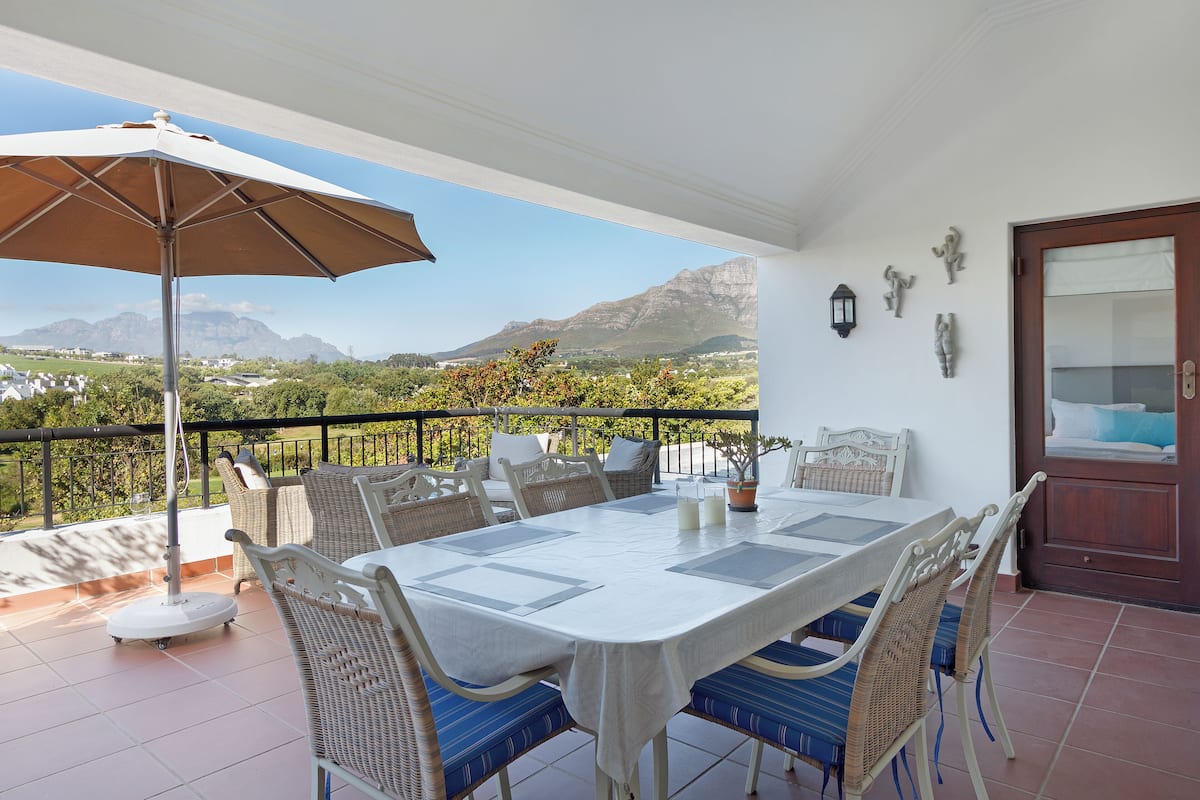 A terrace with a dining table, chairs, and an umbrella.