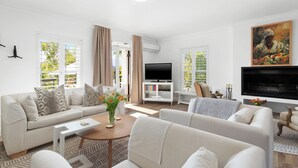 Ein modernes Wohnzimmer mit einer Couch, einem Couchtisch und einem Fernseher. Es gibt Bücherregale und ein Gemälde an der Wand.