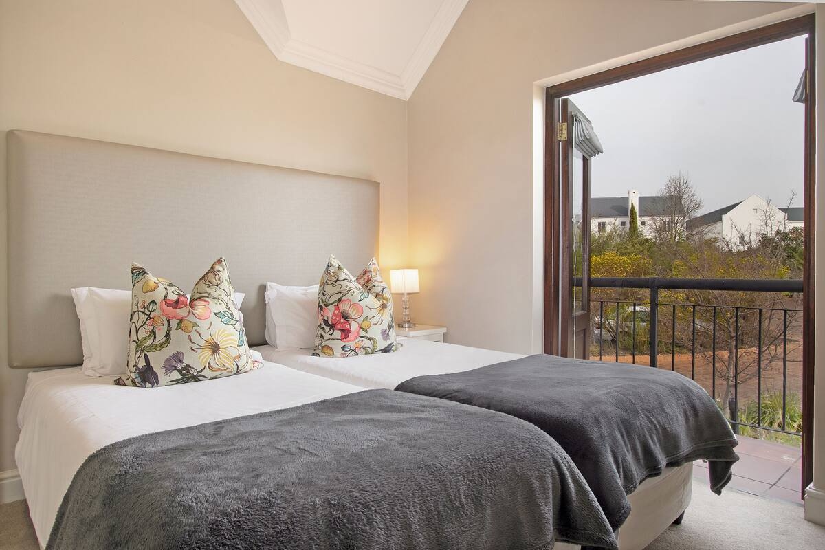 A hotel room with two beds, a balcony with a view of the outside, and a lamp on the nightstand.