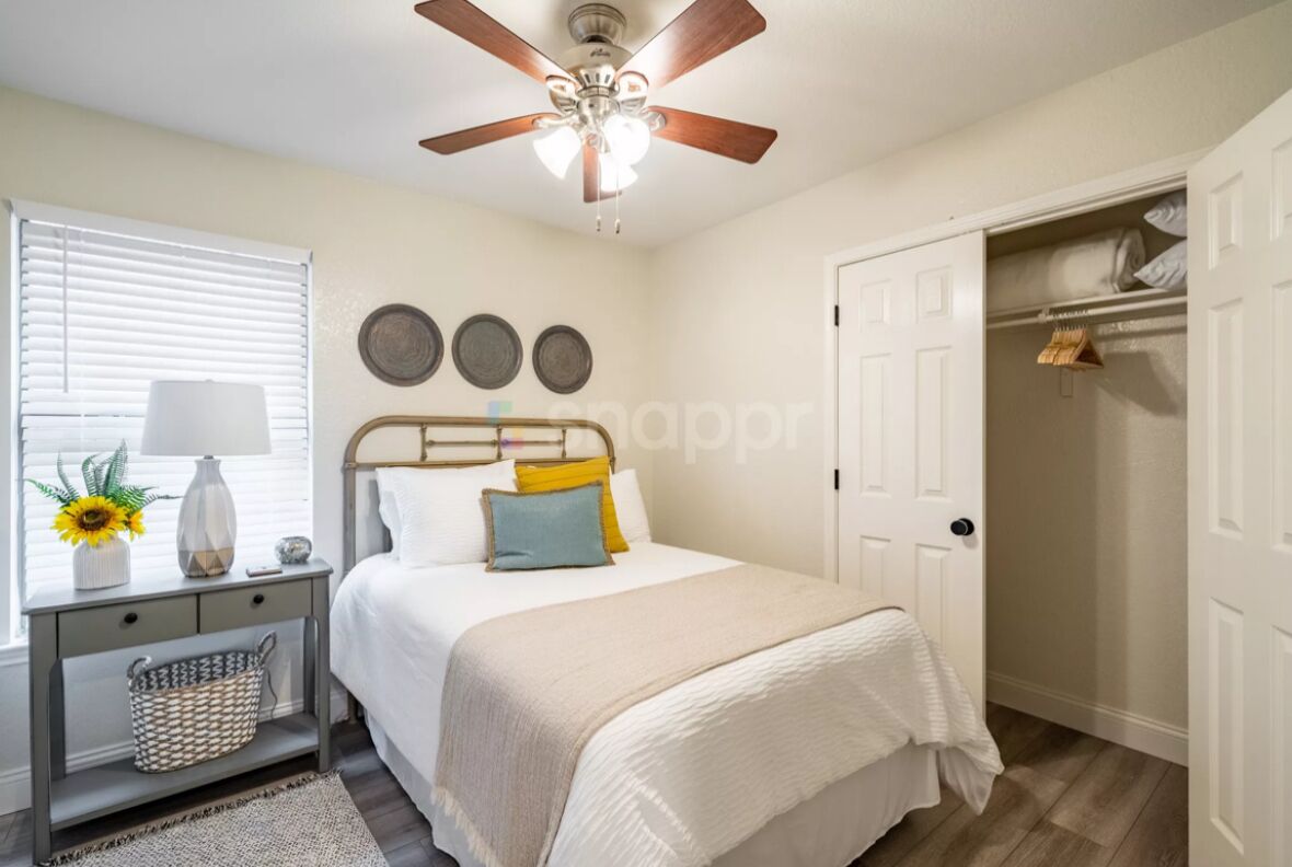 Une chambre à coucher avec un lit, une table de chevet, une lampe et un ventilateur de plafond.