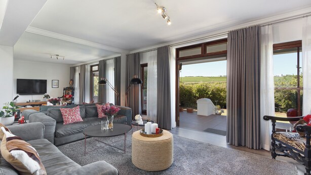 A spacious living room with a grey sofa, a round coffee table, and a large window offering a view of the outdoors. - Winelands Golf Lodges 1 (Cape Town)