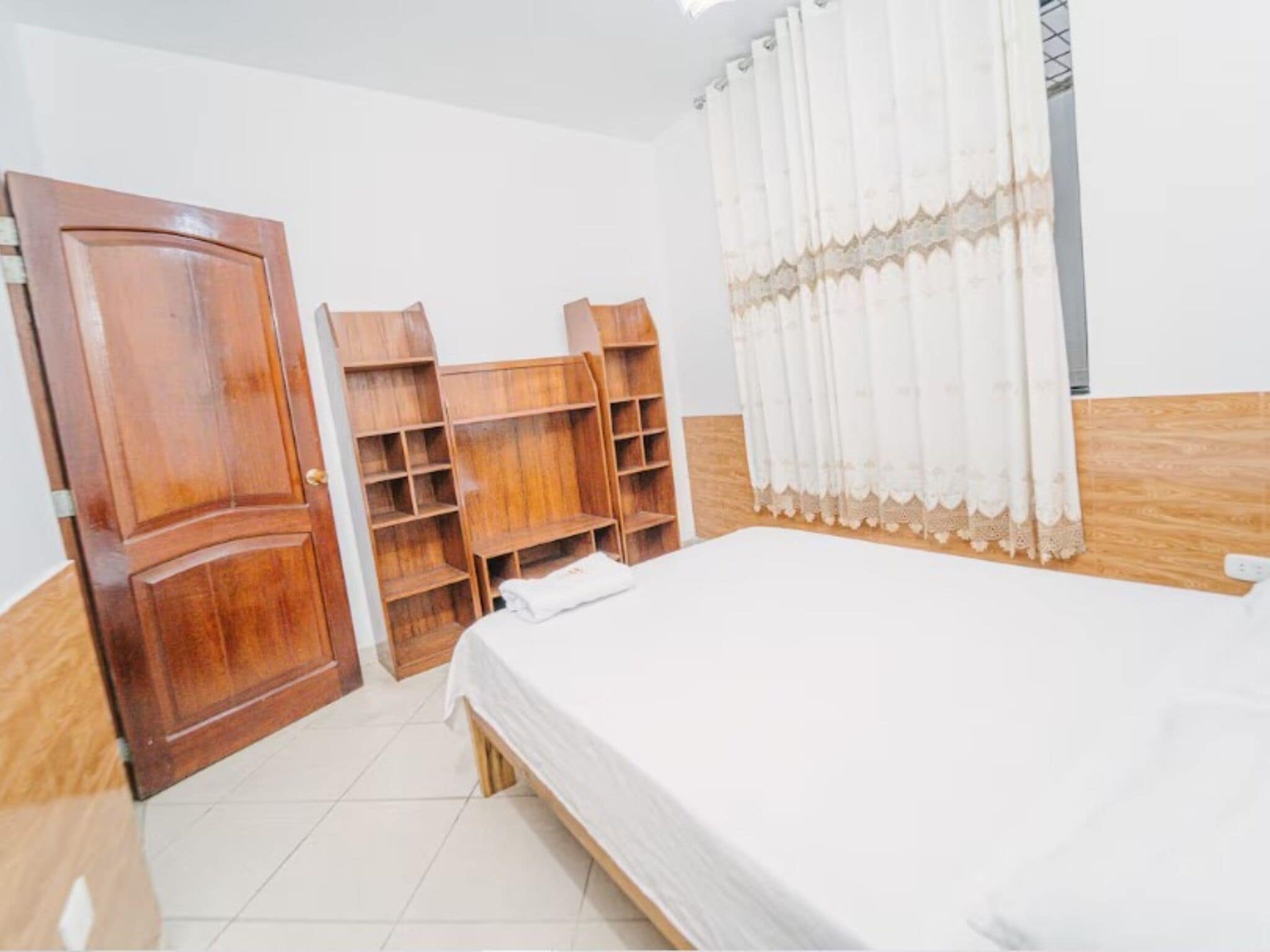 Un dormitorio con una cama de madera, estanterías empotradas y una cortina blanca.
