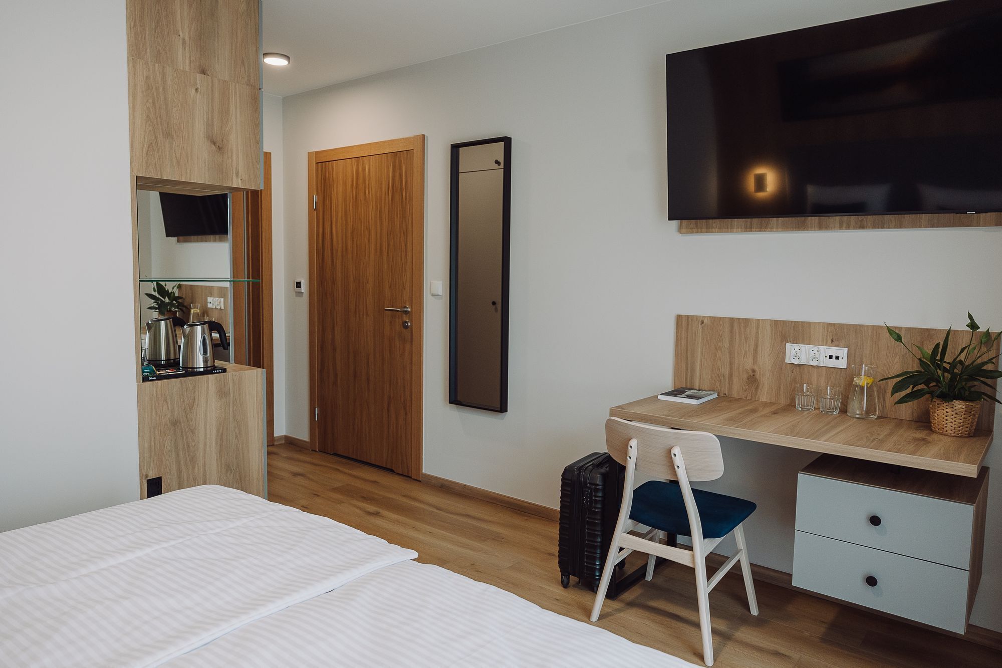 Una habitación de hotel moderna con una cama, un escritorio con una silla, un televisor montado en la pared y un armario de madera.