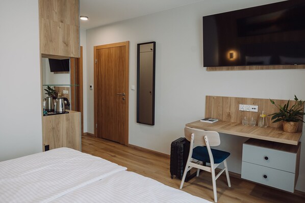 Una habitación de hotel moderna con una cama, un escritorio con una silla, un televisor montado en la pared y un armario de madera.