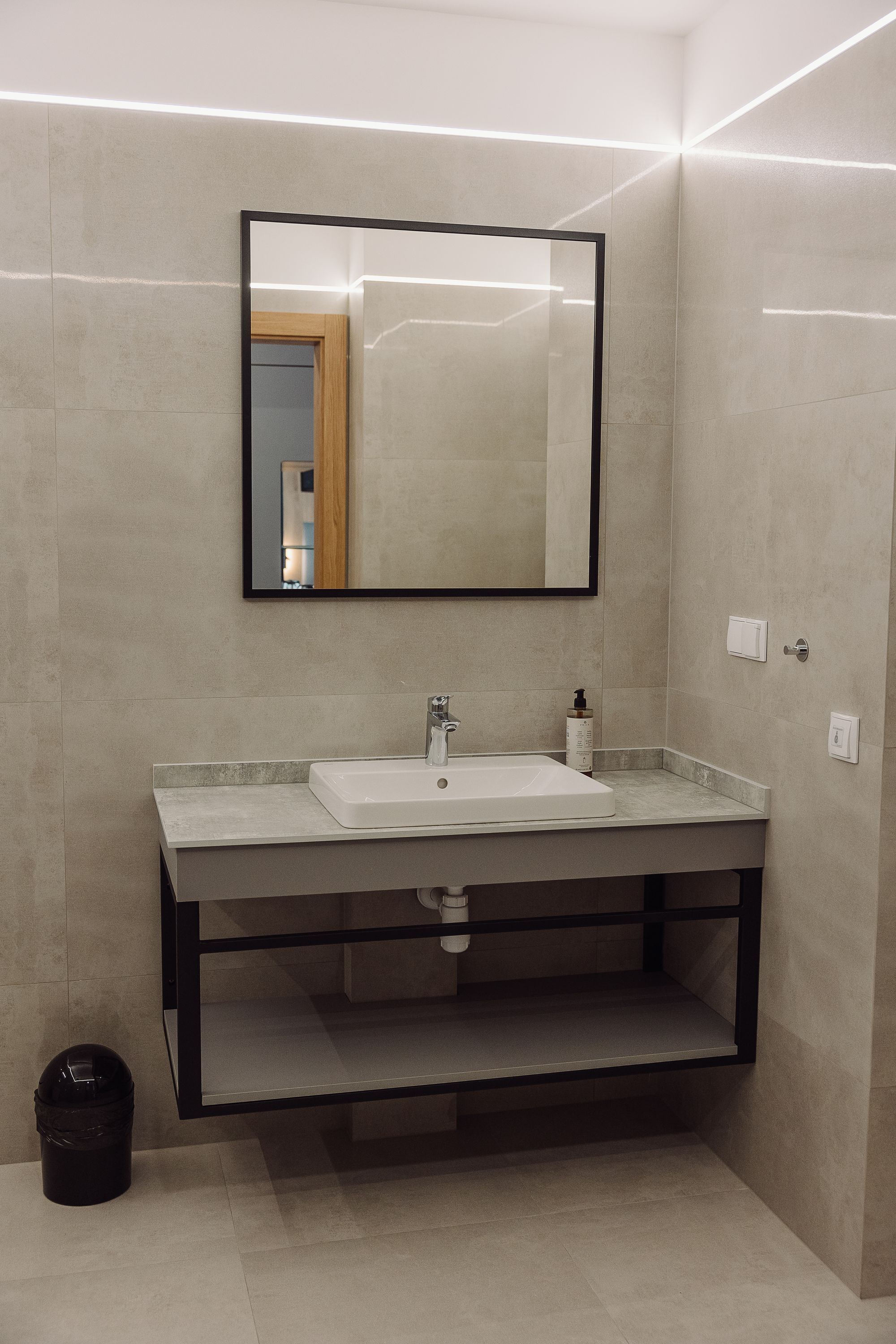 A modern bathroom with a white sink, a mirror, and a black-framed shelf.