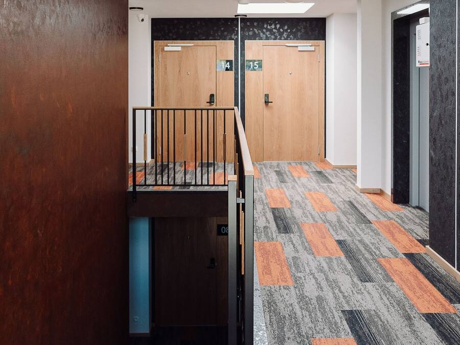 A modern interior with a wooden wall, a staircase, a patterned carpet, and a ceiling light fixture.