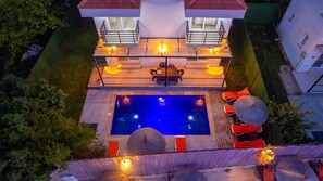 Una piscina en la azotea con barandilla de vidrio, mobiliario exterior y una escalera que conduce a una terraza superior.