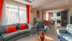 A modern living room with a grey sofa, orange cushions, a coffee table with a vase, and a dining area with orange chairs. - SUREYYA HOTEL BY KALIPSO (Fethiye)