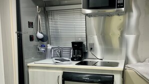 A compact kitchenette with a microwave, coffee maker, and dishwasher. - Iconic Airstream River Glamping (Belton)