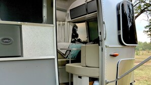 A recreational vehicle with an open rear door, revealing a sleeping area with a bed and curtains. - Iconic Airstream River Glamping (Belton)