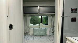 A compact bedroom with a bed, a window, and a control panel. - Iconic Airstream River Glamping (Belton)