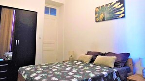 A bedroom with a bed, pillows, a nightstand, a lamp, a wardrobe, and a ceiling light.