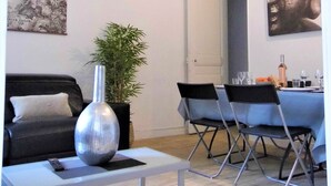 A modern living room with a sofa, a coffee table, a dining table with chairs, a large vase, and artwork on the walls.